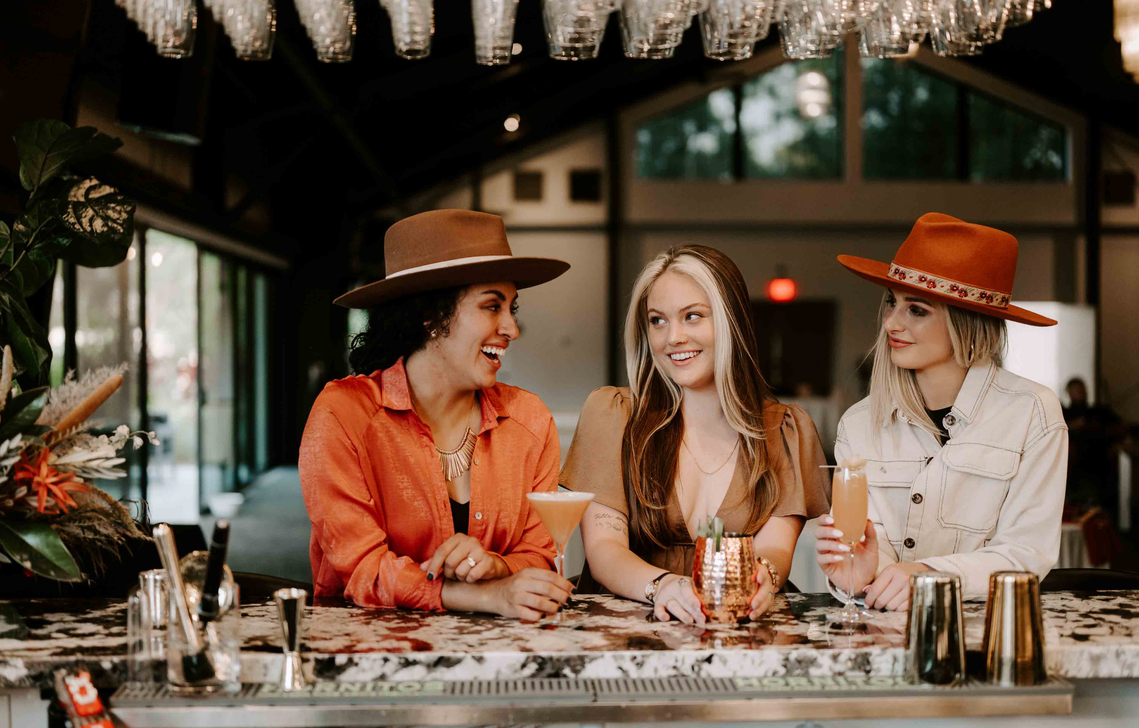 three women sitting at the bar drinking cocktails