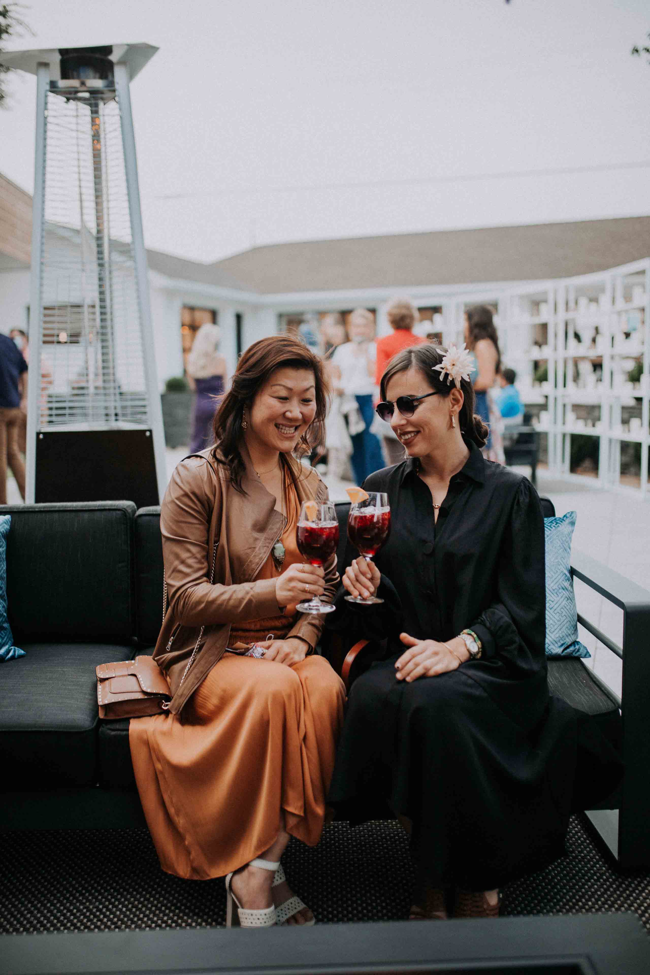 two girls sitting on a sofa at an event while cheersing their drinks 1
