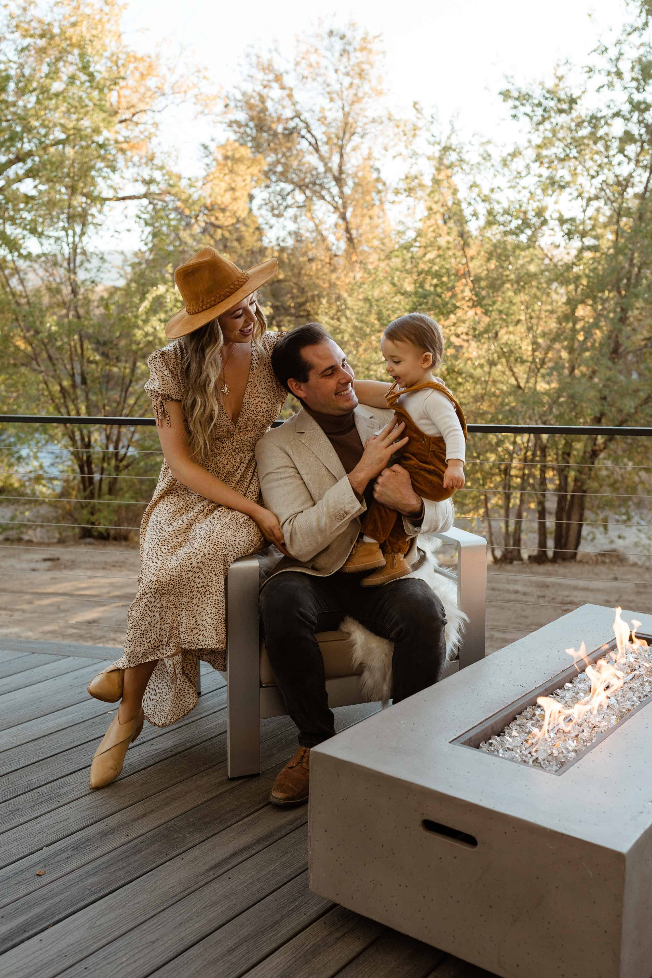 Family of three sitting in a chair by a fire pit outside