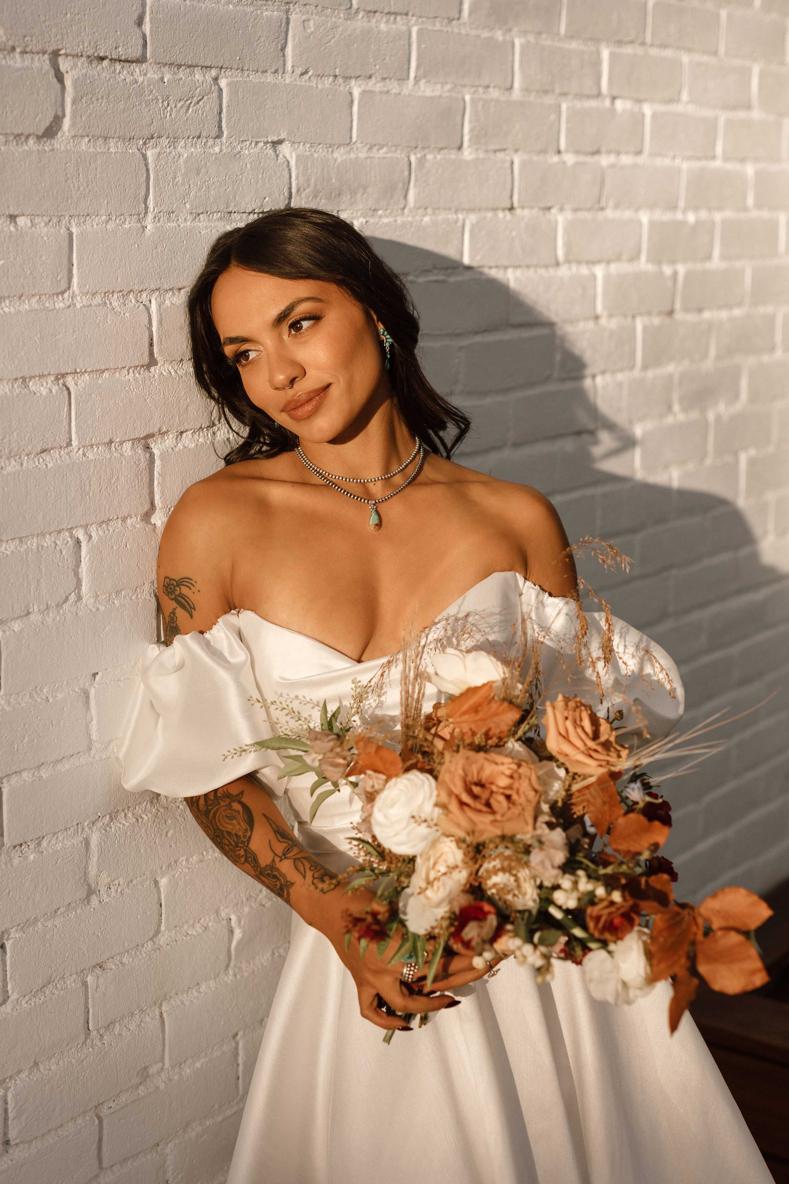 a bride standing against a white brick wall and holding a bouquet