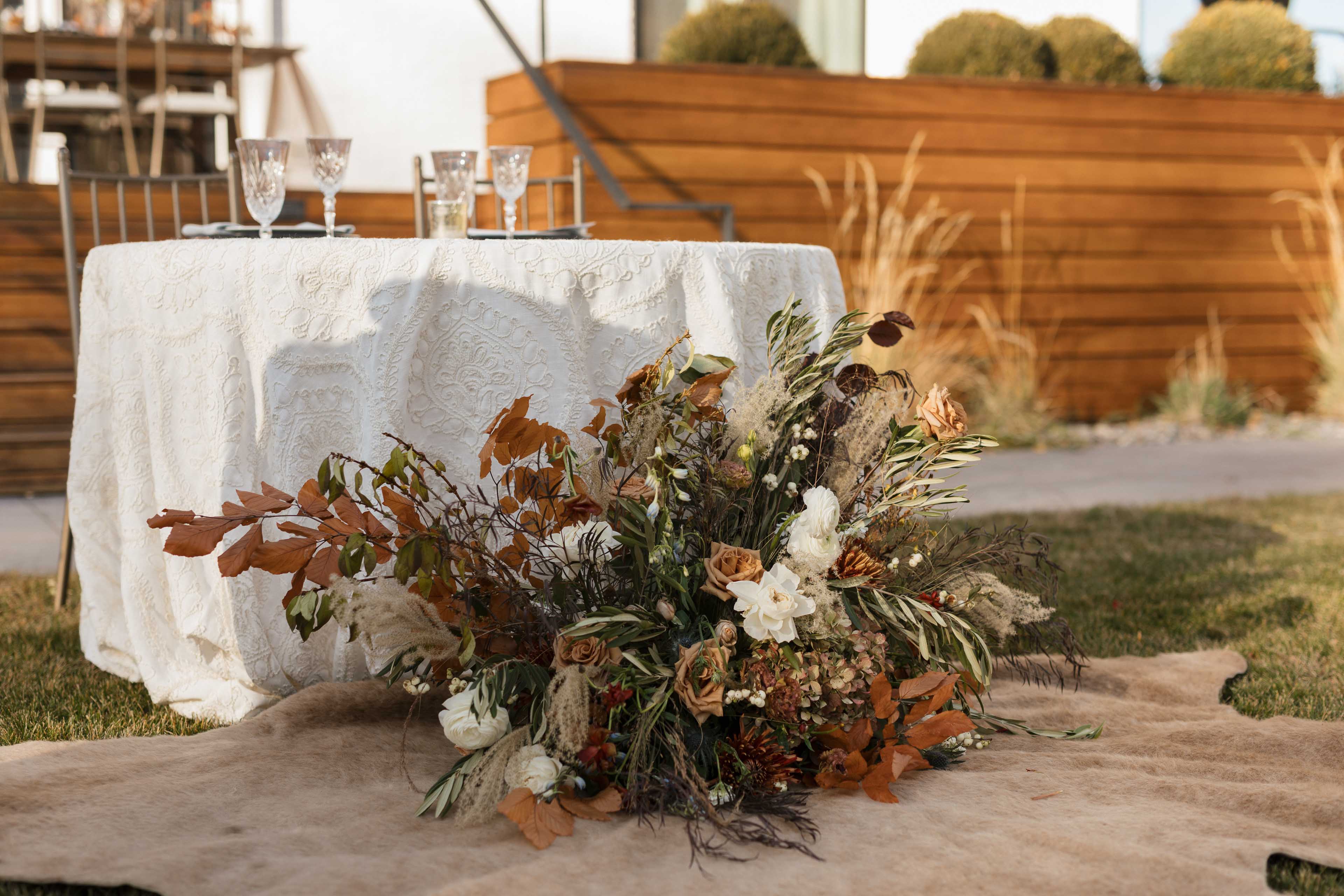 a large fall colored floral arrangement on the ground at the base of a table