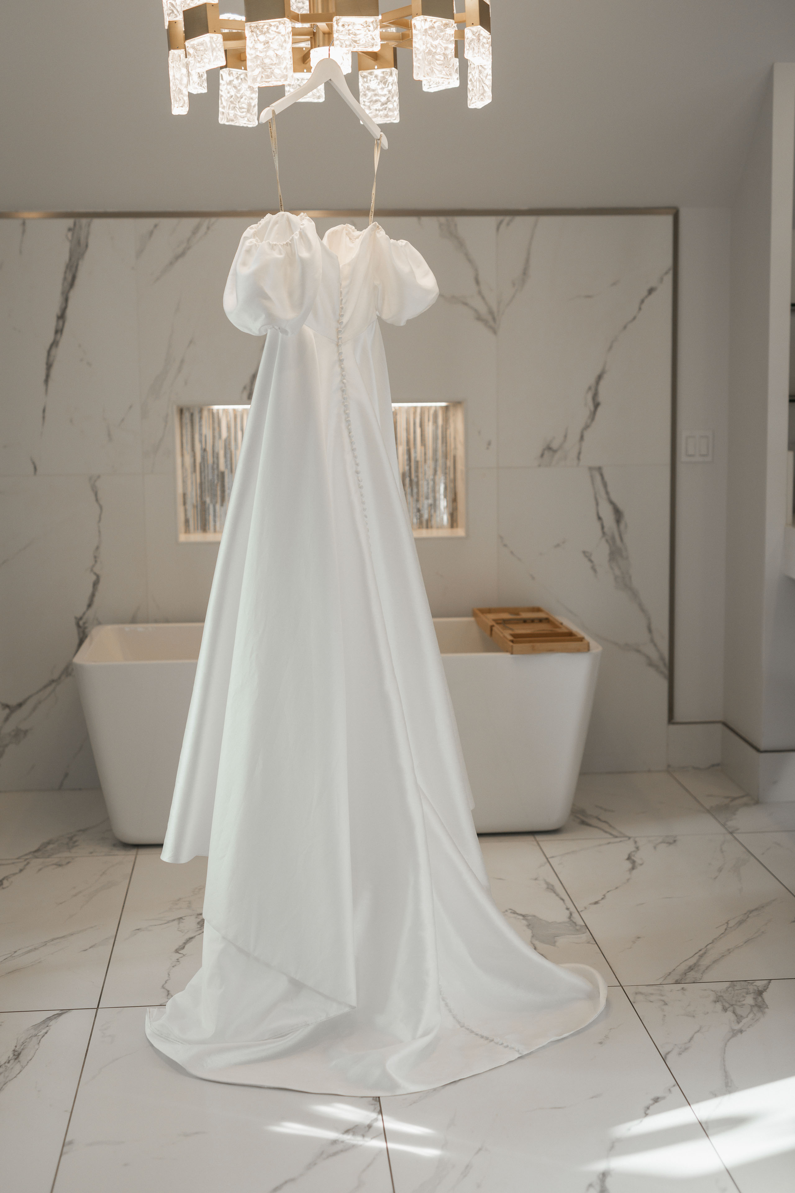 a wedding dress hanging from a chandelier in a room with white marble