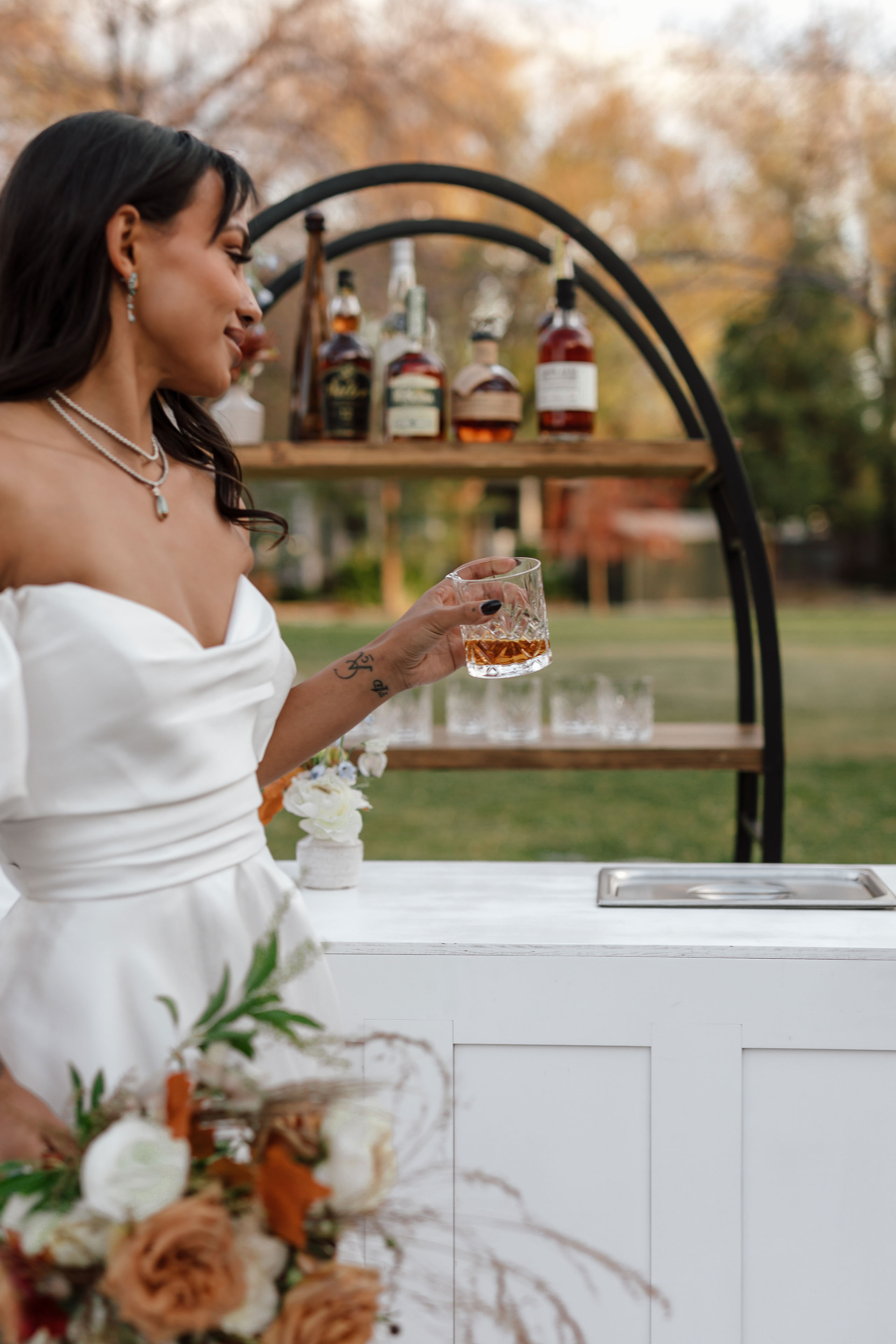 a woman holding a glass of whiskey near an outdoor bar