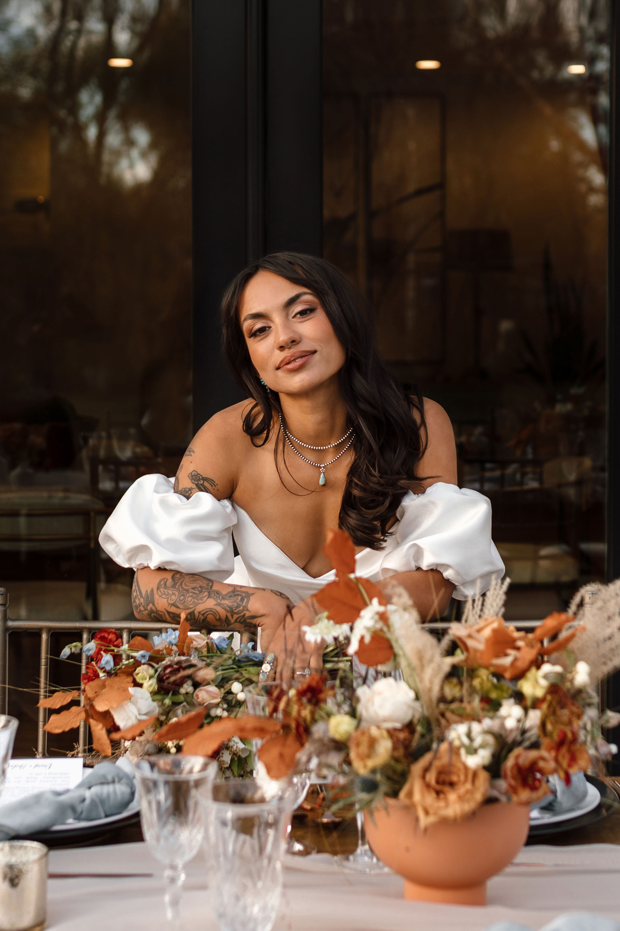 a woman standing a table thats decorated with fall colored flowers
