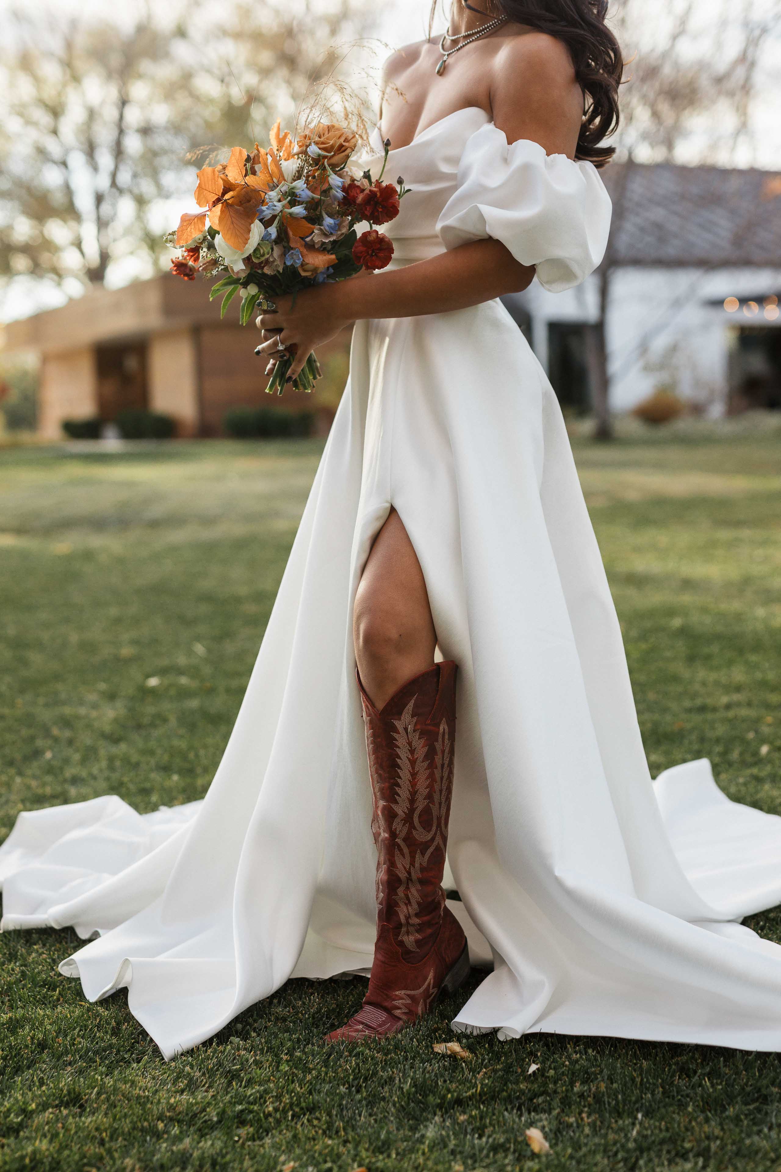 a woman wearing a white gown red cowboy boots and holding a fall colored bouquet