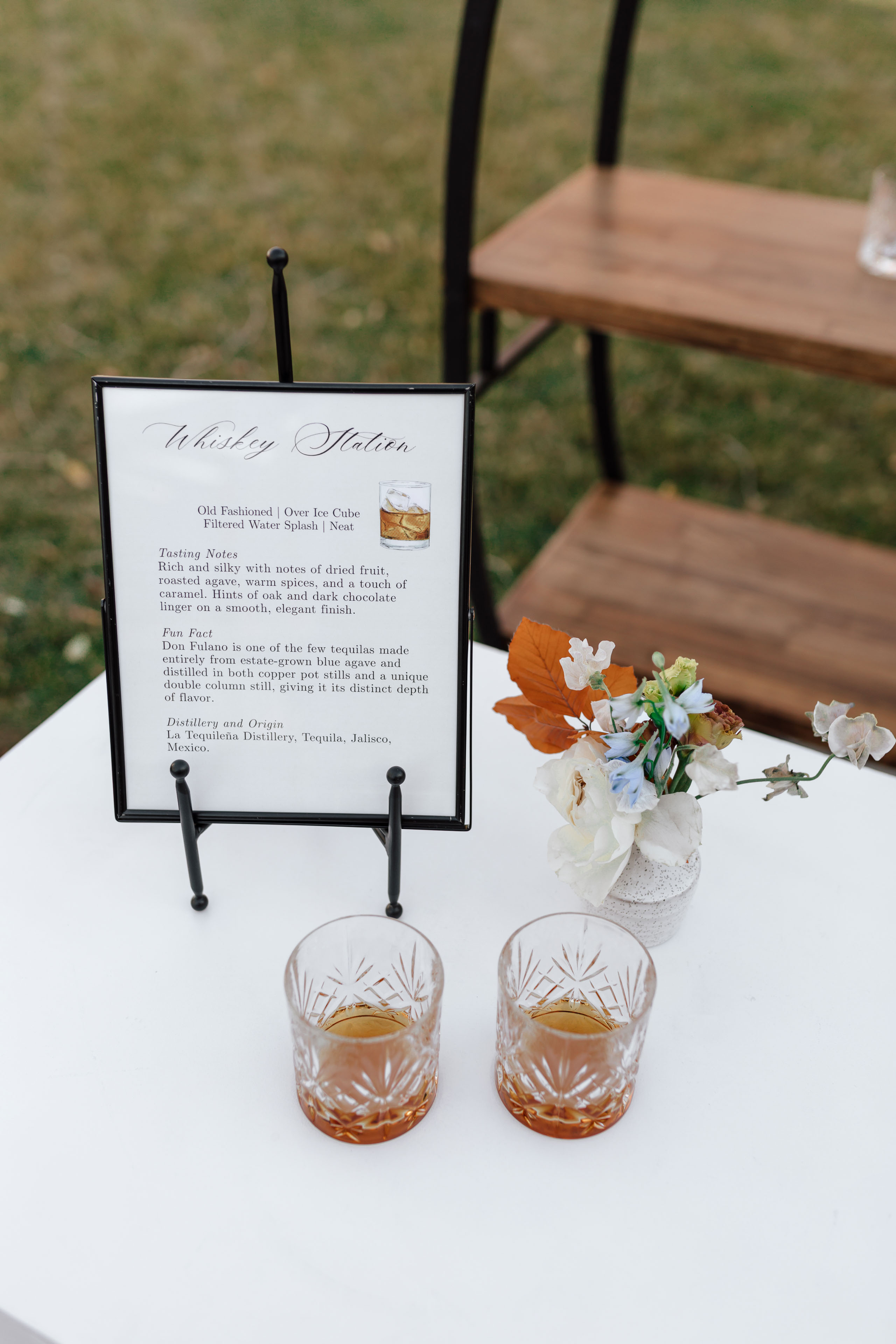two glasses of whiskey on a white table with a sign that describes that says whiskey station